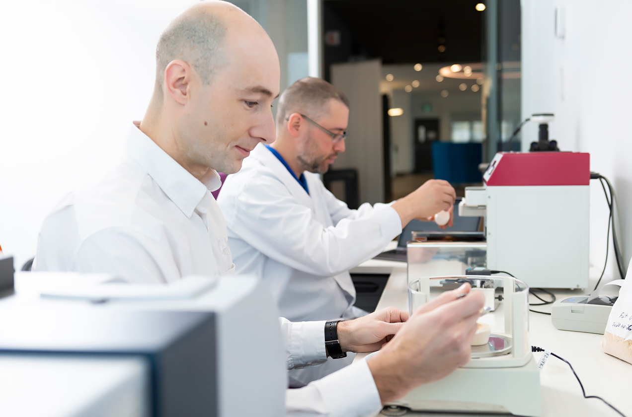 Two lab specialists test animal nutrition ingredients using precision analytical equipment.