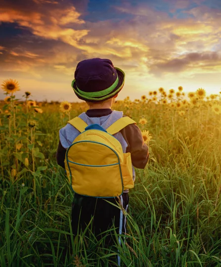 Child with yellow backpack facing a sunflower field at sunset, symbolizing research and a sustainable future.