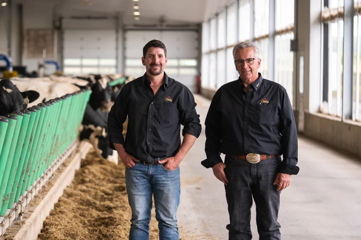 Two dairy producers in a modern barn, highlighting their collaboration with Jefo in animal nutrition solutions.