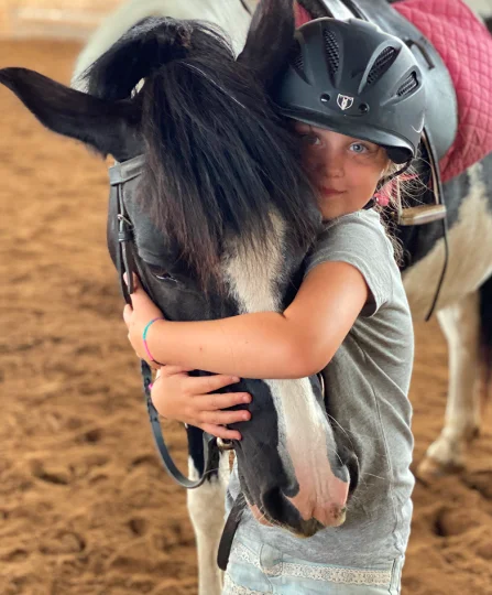 Young girl hugging a saddled horse in an arena, highlighting the human-animal bond in equine nutrition.