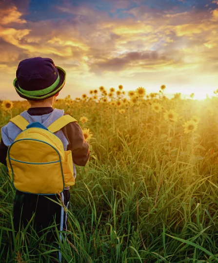 Child with yellow backpack in sunflower field at sunset, symbolizing future and sustainable commitment.