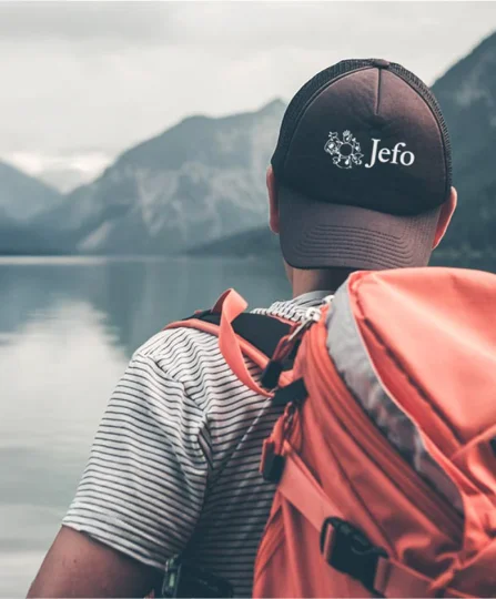 Jefo team member with backpack facing a mountain lake — symbolizing adventure and mobility in animal nutrition.