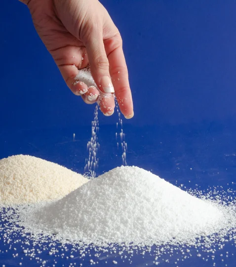 Hand sprinkling white granules on blue background, illustrating ingredient protection technology in animal nutrition.